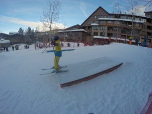Young skiier rides a box at Winter Park Resort Mini Railjam