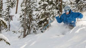 Skier blows up powder while making turns through the trees