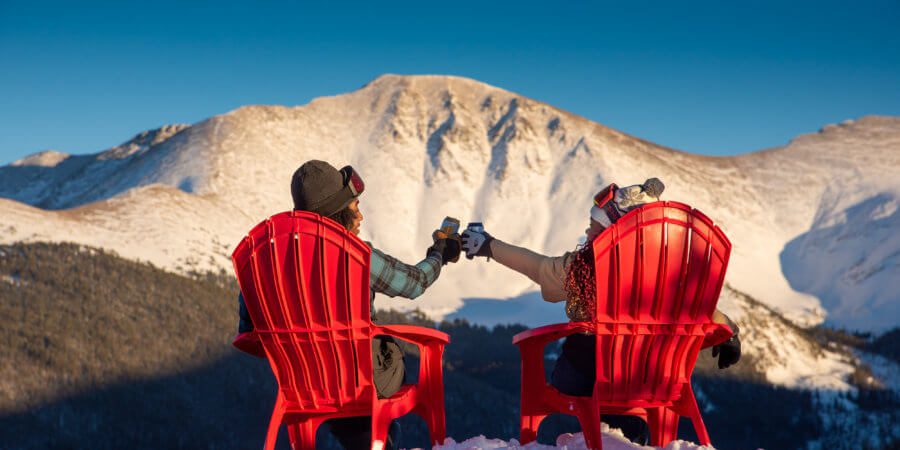 Two seated people raise a cheers in front of a snowy mountain peak.